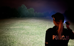 policjantka stojąca tyłem w ręku trzyma latarkę i oświetla park