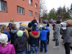 Fotografia kolorowa. Policjant z grupą dzieci przed komendą.