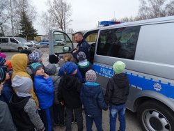 Fotografia kolorowa. Policjant pokazuje dzieciom wnętrze radiowozu.