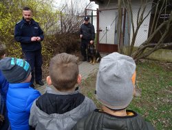 Fotografia kolorowa. Policjant pokazuje dzieciom przewodnika i psa służbowego.