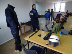 Fotografia kolorowa. Policjant pokazuje dzieciom wyposażenie policjanta do służby.