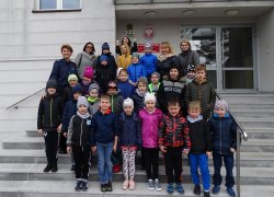 Fotografia kolorowa. Zdjęcie grupowe dzieci zwiedzających komendę, na schodach przed jednostka policji.