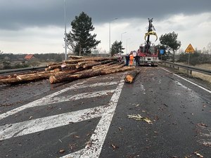 Na zdjęciu ciężarówka z rozsypanym drewnem na drodze