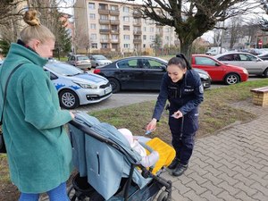 Policjantka pochylająca się do dziecka w wózku prowadzonego przez mamę.