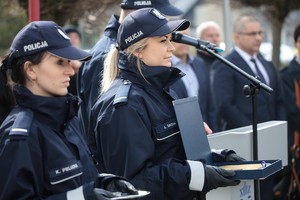 Na zdjęciu są dwie policjantki. Pierwsza  na rękach położoną ma tackę z kluczykiem od nowego radiowozu, obok stoi druga policjantką, która w rękach trzyma symboliczny klucz do otwarcia nowego posterunku.