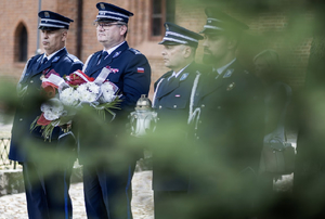4 funkcjonariuszy policji, jedne trzyma bukiet kwiatów drugi od prawej trzyma znicz