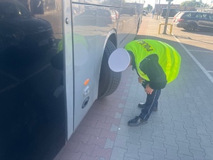 policjant oglądający stan opon w autobusie